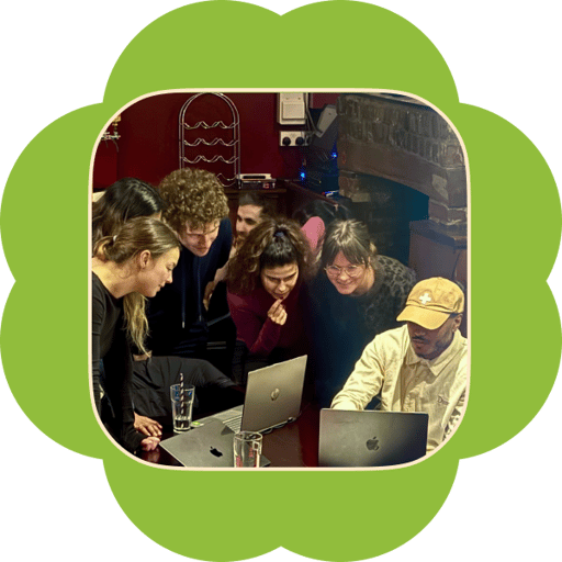 A group leaning in around laptops at a bar table, learning from each other